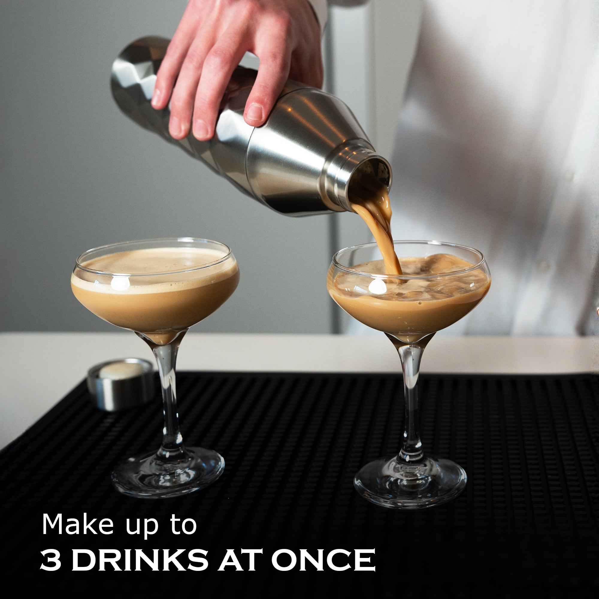 Person pouring a drink from a shaker into two glasses on a bar counter.